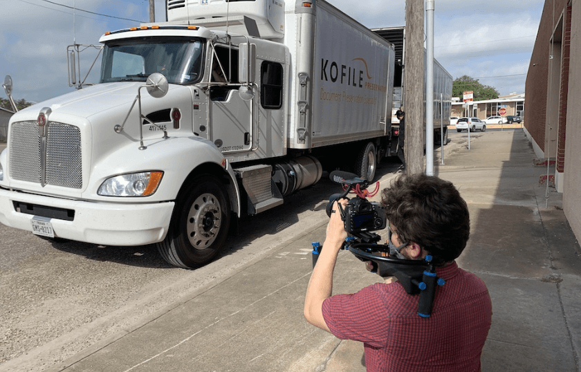 A man holding a professional video camera pointing it at a corporate delivery truck